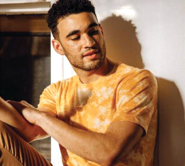 Man wearing orange tie dye t-shirt sitting against wall