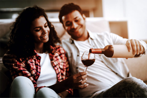 Man sitting next to woman while pouring wine into her glass