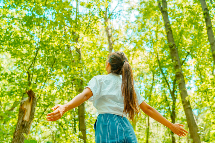 woman breathing in clean air in nature, arms outstretched looking up toward sky