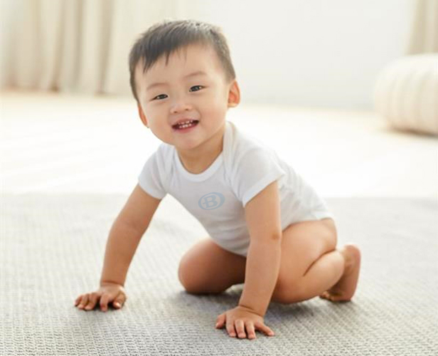 infant on floor smiling wearing bodysuit