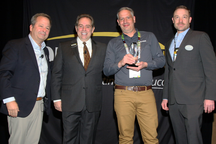 four men lined up smiling, one holding an award