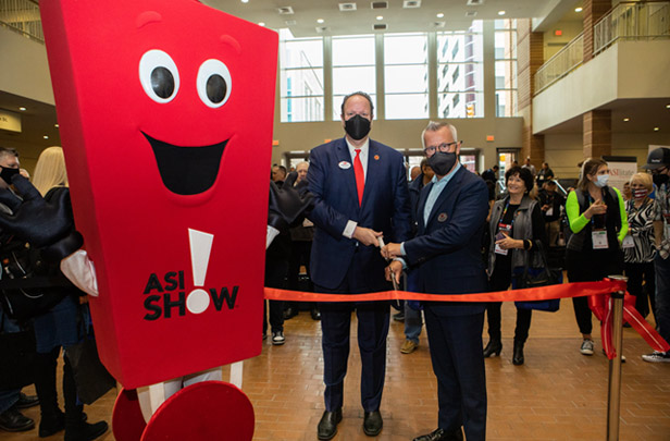 Matthew Cohn and Tim Andrews cutting red ribbon to start ASI Show, standing next to red Promo