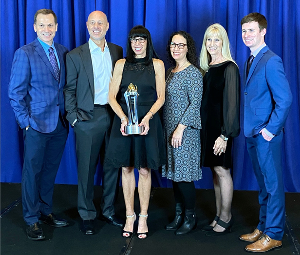 The Book Company team in front on blue curtain, woman in middle holding award