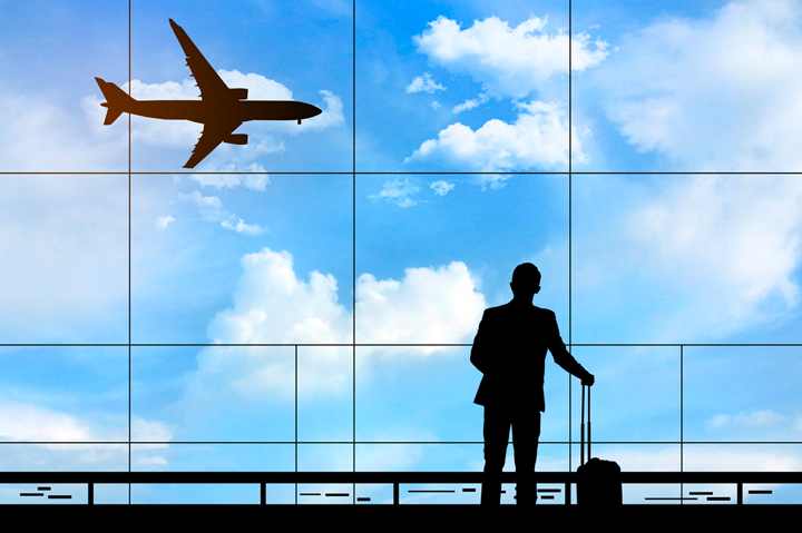 silhouette of business man at airport, looking out window, plane flying against blue sky