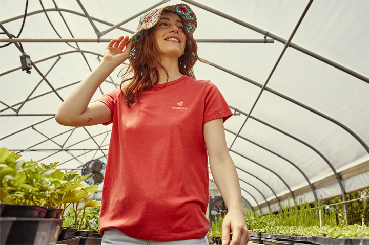 woman standing in greenhouse wearing red t-shirt and bucket hat